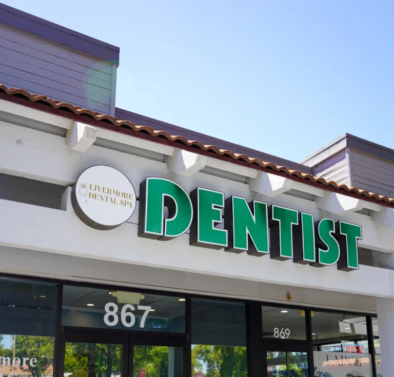 The clean exterior storefront of Livermore Dental Spa featuring a large green Dentist sign above the main glass entrance doors in Livermore, CA.